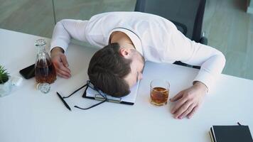Alcoholism, drinking concept. Drunk employee sleeping at working place, holding glass with alcohol video