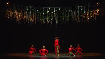 Dancers in red performing on stage with golden streamers in the background. video