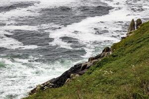Rough Seas Crashing Against Green Cliffs on a Cloudy Day, in Ireland photo
