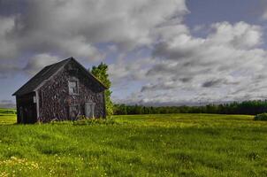 Old Wooden Barn in a Field of Green Grass Under a Cloudy Sky in St-Ludger, Quebec, Canada photo