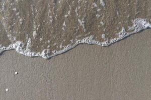 The calm wave of the sea with foam on the beach sand photo