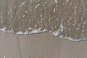 The calm wave of the sea with foam on the beach sand photo