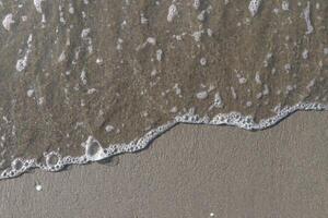 The calm wave of the sea with foam on the beach sand photo