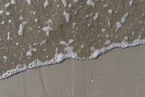 The calm wave of the sea with foam on the beach sand photo