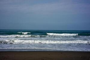 powerful foamy sea waves rolling and splashing over water surface against cloudy blue sky photo