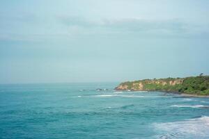 panorama of the scenic view of the beach from a green cliff with very large sea waves. at santolo beach, west java, indonesia photo