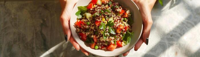 Hands holding a bowl of fresh, colorful quinoa salad with vegetables, perfect for a healthy and nutritious meal. photo