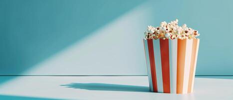 A bucket of popcorn in red and white striped container with dramatic lighting, representing a cinematic experience against a blue background. photo