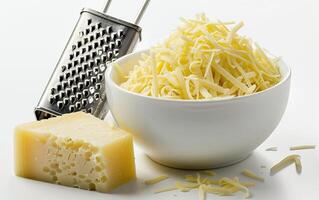 Bowl of shredded cheese with cheese block and grater on white background, perfect for cooking and recipe illustrations. photo