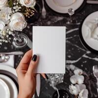 Blank paper card in hand over blurred elegant table setting background. photo
