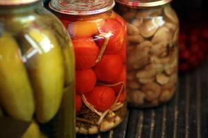 Row of jars with pickled tomatoes, cucumbers and mushrooms standing on black wooden floor photo