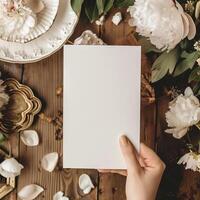 Blank paper in woman's hand over the wooden table with flowers and petals. Flat lay, top view. Space for text. photo