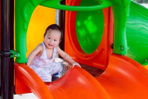 Portrait of A happy toddler boy playing on a playground orange slide, in the summer or spring, enjoying on sunny day. Child aged one year old. photo
