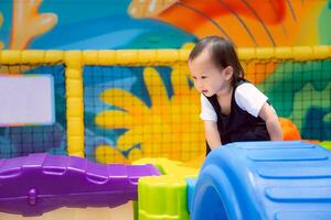 Asian little child is smiling and having fun climbing on toys in an indoor playground. Boy learning through play, leisure activities, muscle development, one year five month old kid. photo
