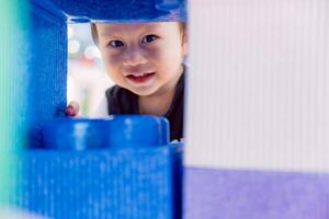 Smiling little child behind large building blocks, baby boy having fun playing hide and seek, adorable Asian child one year and five months old. Helps in developing large muscle skills. Copy space. photo