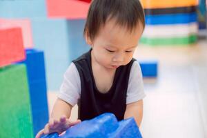 A toddler joyfully playing with colorful toy blocks at home. Little boy building tower of block toys. Educational game for baby and toddler. Children build toy house. photo