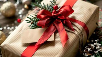A beautifully wrapped present with a red bow and a blank gift tag sits on a wooden table scattered with ornaments and pine cones. photo