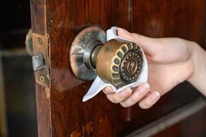 Close up of woman hand cleaning doorknob with antibacterial disinfecting wipe for killing virus or bacteria on touching surfaces or touching public handle. Conceptual of prevention in public health. photo