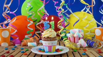 Birthday 51 cupcake with candles burning on rustic wooden table with background of colorful balloons, plastic cups and candies with blue wall in the background photo