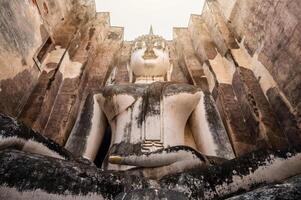 An iconic huge Buddha statue in a roofed building of Wat Si Chum temple located in the North zone of the Sukhothai Historical Park outside the walled city. photo