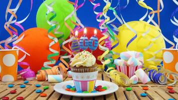 Birthday 400 cupcake with candles burning on rustic wooden table with background of colorful balloons, plastic cups and candies with blue wall in the background photo