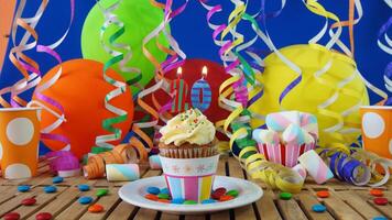 Birthday 20 cupcake with candles burning on rustic wooden table with background of colorful balloons, plastic cups and candies with blue wall in the background photo