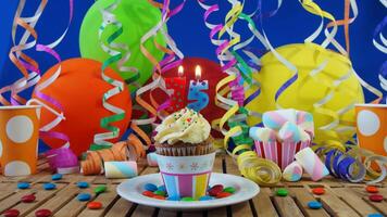 Birthday 75 cupcake with candles burning on rustic wooden table with background of colorful balloons, plastic cups and candies with blue wall in the background photo