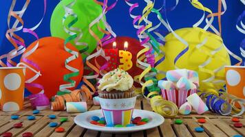 Birthday 73 cupcake with candles burning on rustic wooden table with background of colorful balloons, plastic cups and candies with blue wall in the background photo