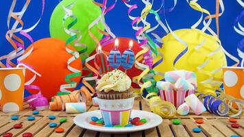 Birthday 200 cupcake with candles burning on rustic wooden table with background of colorful balloons, plastic cups and candies with blue wall in the background photo