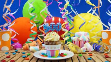Birthday 500 cupcake with candles burning on rustic wooden table with background of colorful balloons, plastic cups and candies with blue wall in the background photo