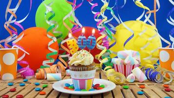 Birthday 300 cupcake with candles burning on rustic wooden table with background of colorful balloons, plastic cups and candies with blue wall in the background photo