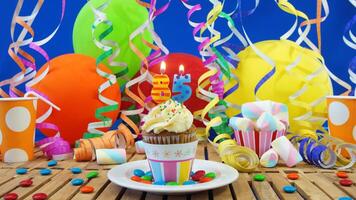 Birthday 85 cupcake with candles burning on rustic wooden table with background of colorful balloons, plastic cups and candies with blue wall in the background photo
