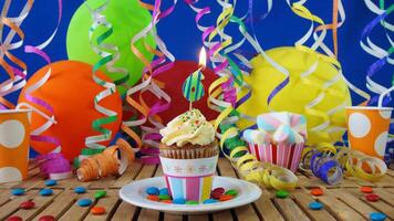 Birthday 6 cupcake with candles burning on rustic wooden table with background of colorful balloons, plastic cups and candies with blue wall in the background photo