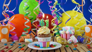 Birthday 61 cupcake with candles burning on rustic wooden table with background of colorful balloons, plastic cups and candies with blue wall in the background photo