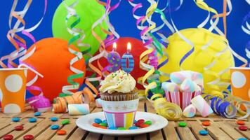 Birthday 90 cupcake with candles burning on rustic wooden table with background of colorful balloons, plastic cups and candies with blue wall in the background photo