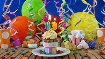 Birthday 63 cupcake with candles burning on rustic wooden table with background of colorful balloons, plastic cups and candies with blue wall in the background photo