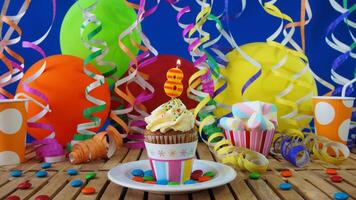 Birthday 8 cupcake with candles burning on rustic wooden table with background of colorful balloons, plastic cups and candies with blue wall in the background photo