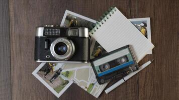 Old photo camera surrounded by photographs of women in different places, map, notebook and music cassette on a dark wooden table