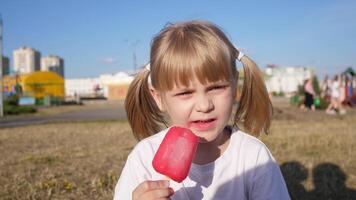 Portrait of a little beautiful Slavic girl eating ice cream in a city park in summer against the blue sky photo