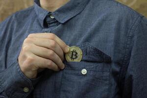 Man puts physical version of Bitcoin in his shirt breast pocket, saving money in cryptocurrency concept, savings and investment photo