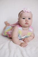Full body figure of an infant looking at the camera while lying on his back on a white sheet bed photo