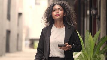 A black woman is getting ready for work in an office uniform in a public downtown area, carrying all her work equipment including a computer and a phone. video