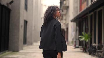A black woman is getting ready for work in an office uniform in a public downtown area, carrying all her work equipment including a computer and a phone. video