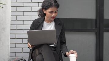 A black woman is getting ready for work in an office uniform in a public downtown area, carrying all her work equipment including a computer and a phone. video