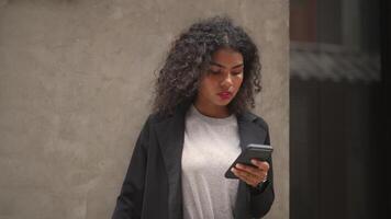 A black woman is getting ready for work in an office uniform in a public downtown area, carrying all her work equipment including a computer and a phone. video