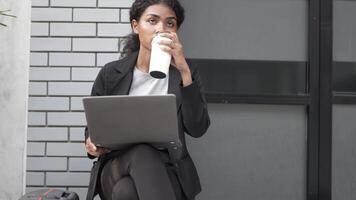 A black woman is getting ready for work in an office uniform in a public downtown area, carrying all her work equipment including a computer and a phone. video