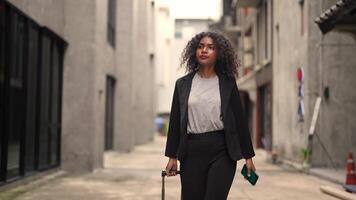 A black woman is getting ready for work in an office uniform in a public downtown area, carrying all her work equipment including a computer and a phone. video