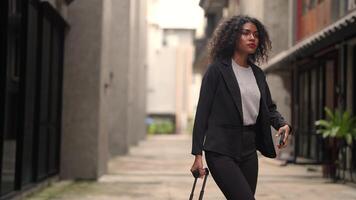 A black woman is getting ready for work in an office uniform in a public downtown area, carrying all her work equipment including a computer and a phone. video