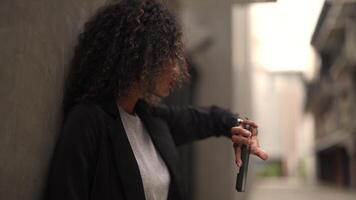 A black woman is getting ready for work in an office uniform in a public downtown area, carrying all her work equipment including a computer and a phone. video