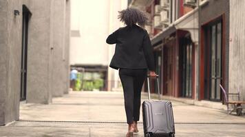 A black woman is getting ready for work in an office uniform in a public downtown area, carrying all her work equipment including a computer and a phone. video